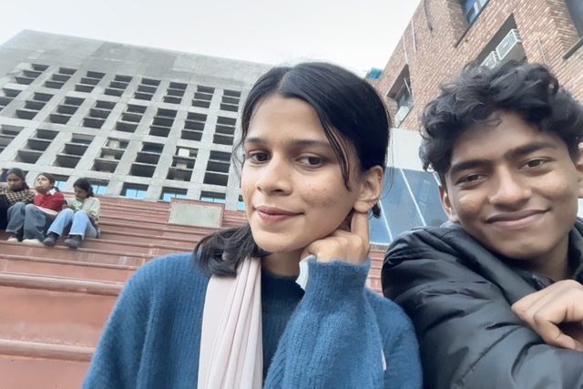 Two friends sitting outdoors near a brick building.