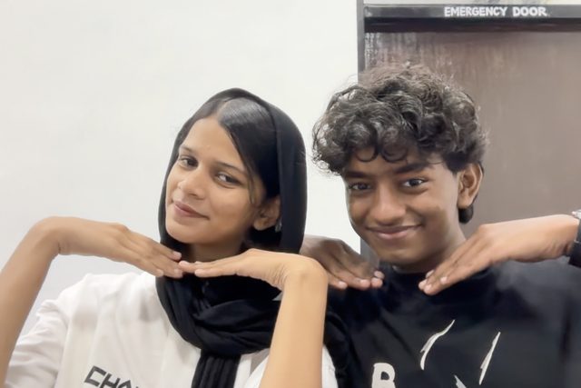 Two friends posing together with their hands near their faces.