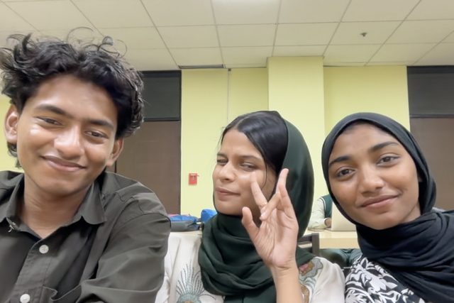 Three people smiling together in an indoor selfie.